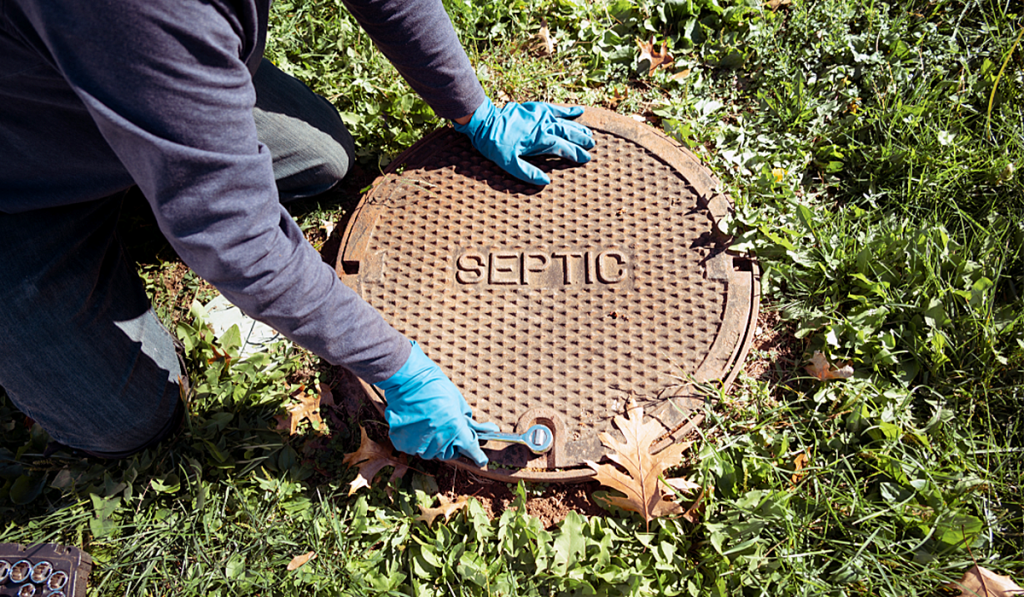 A person holding a metal entrance plate at the entrance of a septic system in the ground