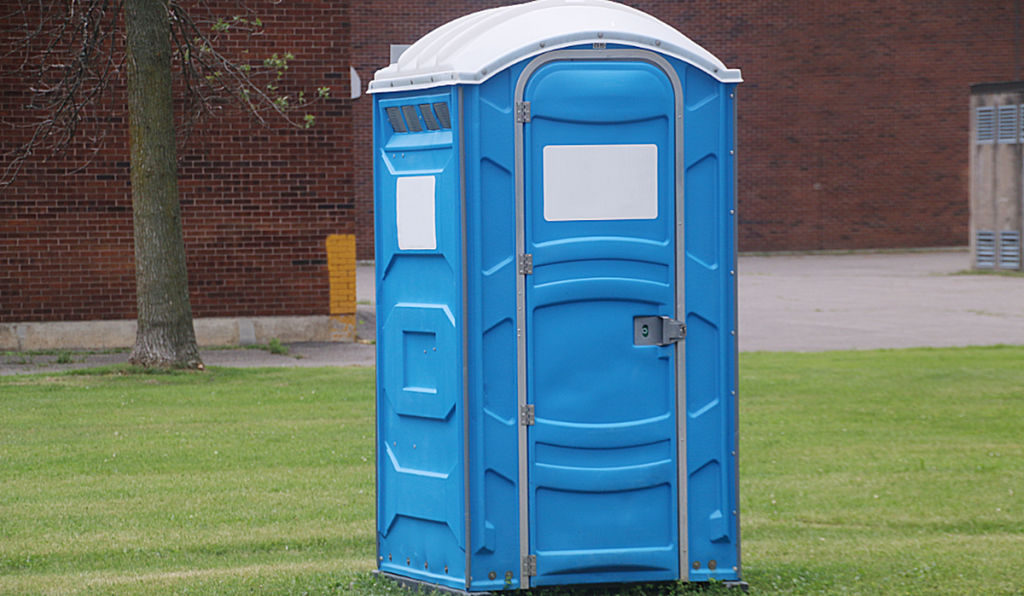 Portable toilet unit positioned outdoors on a grassed area, providing temporary sanitation facilities for events and worksites.