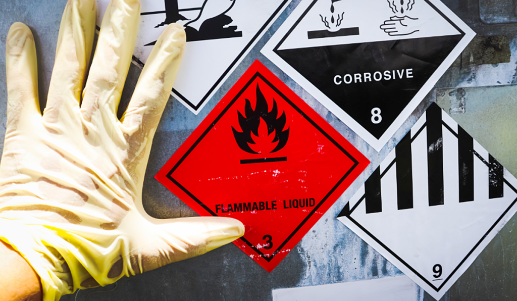 Chemical hazard labels for flammable and corrosive substances displayed alongside protective gloves, highlighting safe chemical handling practices.