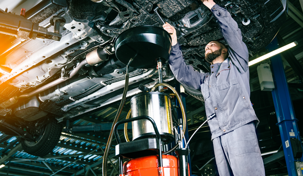 Mechanic draining used engine oil from a vehicle during routine automotive servicing.